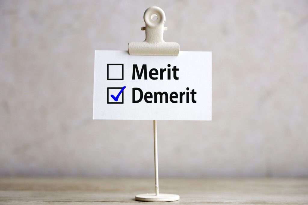 上部がクリップになった白いスタンドに、二つのチェックリストが並んでいる。左には「メリット」、右には「デメリット」が書かれ、デメリットの項目に青いチェックマークが付いている。