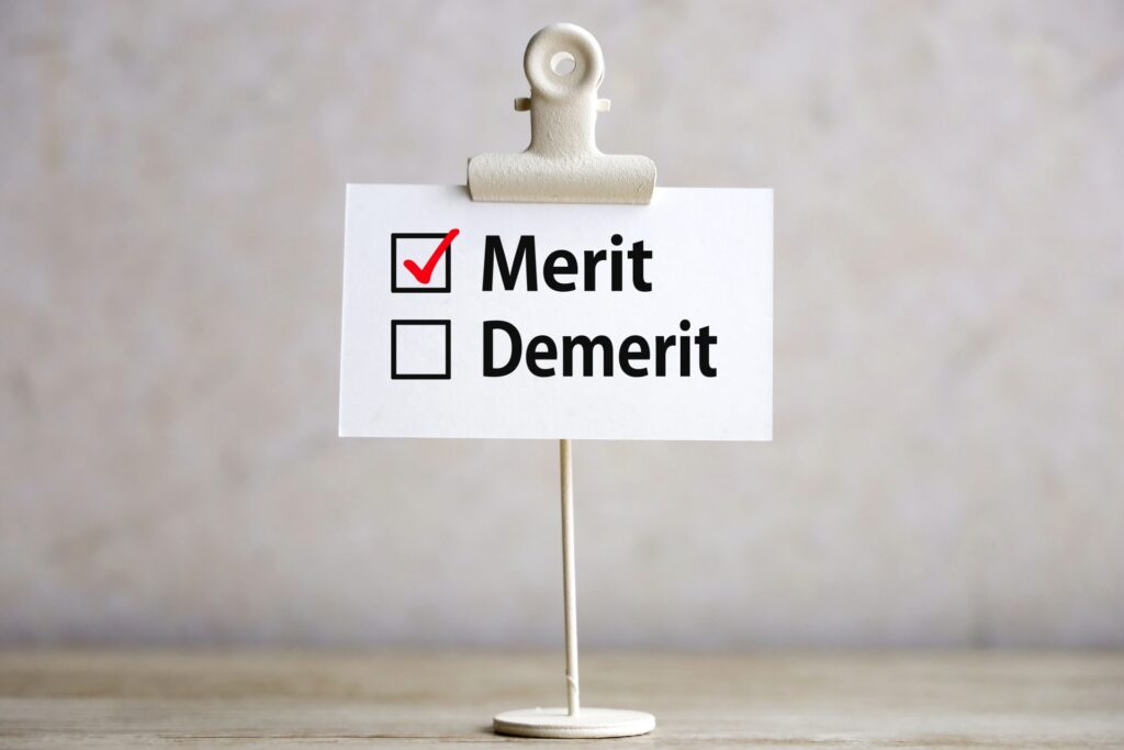 白い細長いスタンドの先に白いクリップがあり、そこに紙が挟まれている。紙には『デメリット』『メリット』と書かれた二つのチェックリストがあり、メリットの欄に赤いチェックマークが入っている。