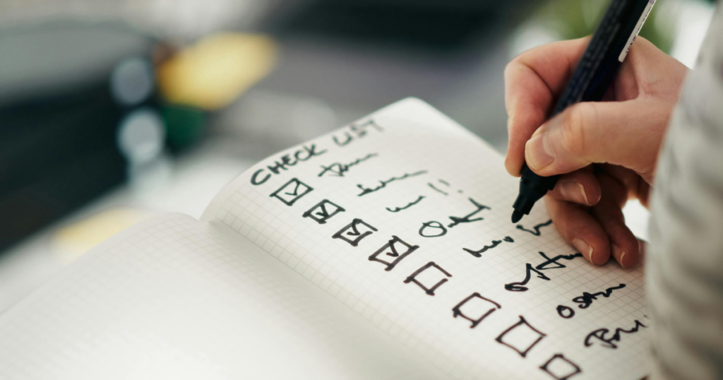 男性がノートの英語チェックリストに書き込み、4項目にチェックが入っている。