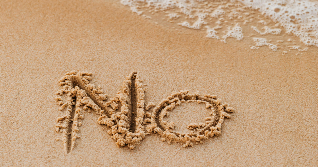 砂浜に「NO」という文字が書かれていて、波がうっすらと寄せて砂に届いている様子。