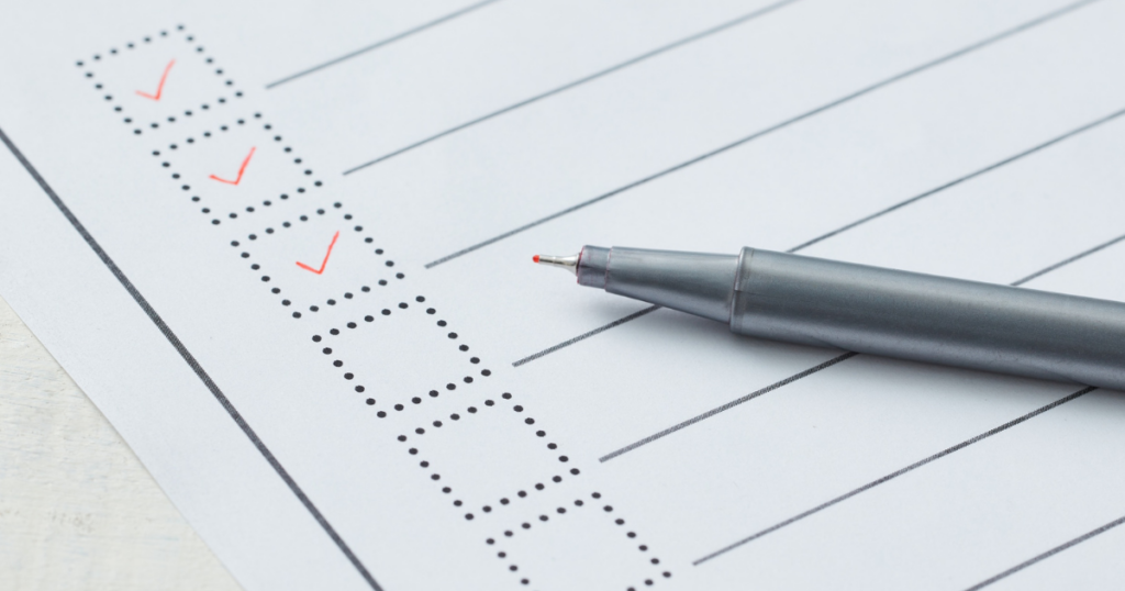 紙に細かいチェックリストが並び、赤いペンで三つチェックが入り、右下に緑のペン先が置かれている。